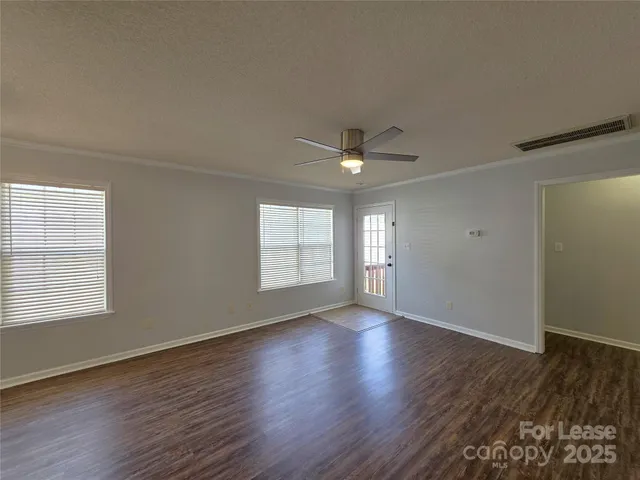 an empty room with wooden floor chandelier fan and windows