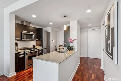 a kitchen with stainless steel appliances kitchen island granite countertop a stove a microwave a dining table and chairs with wooden floor