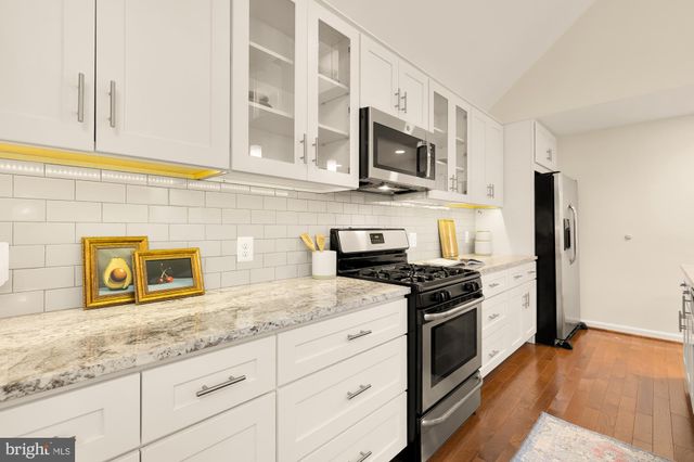 a large white kitchen with a stove a sink a refrigerator and a dining table with wooden floor