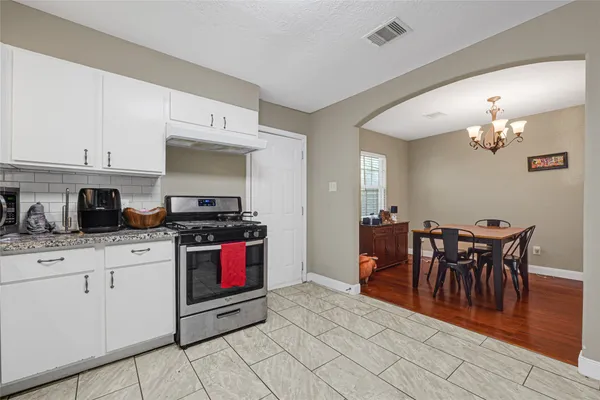 a kitchen with stainless steel appliances granite countertop a stove top oven a sink a dining table and chairs with white cabinets