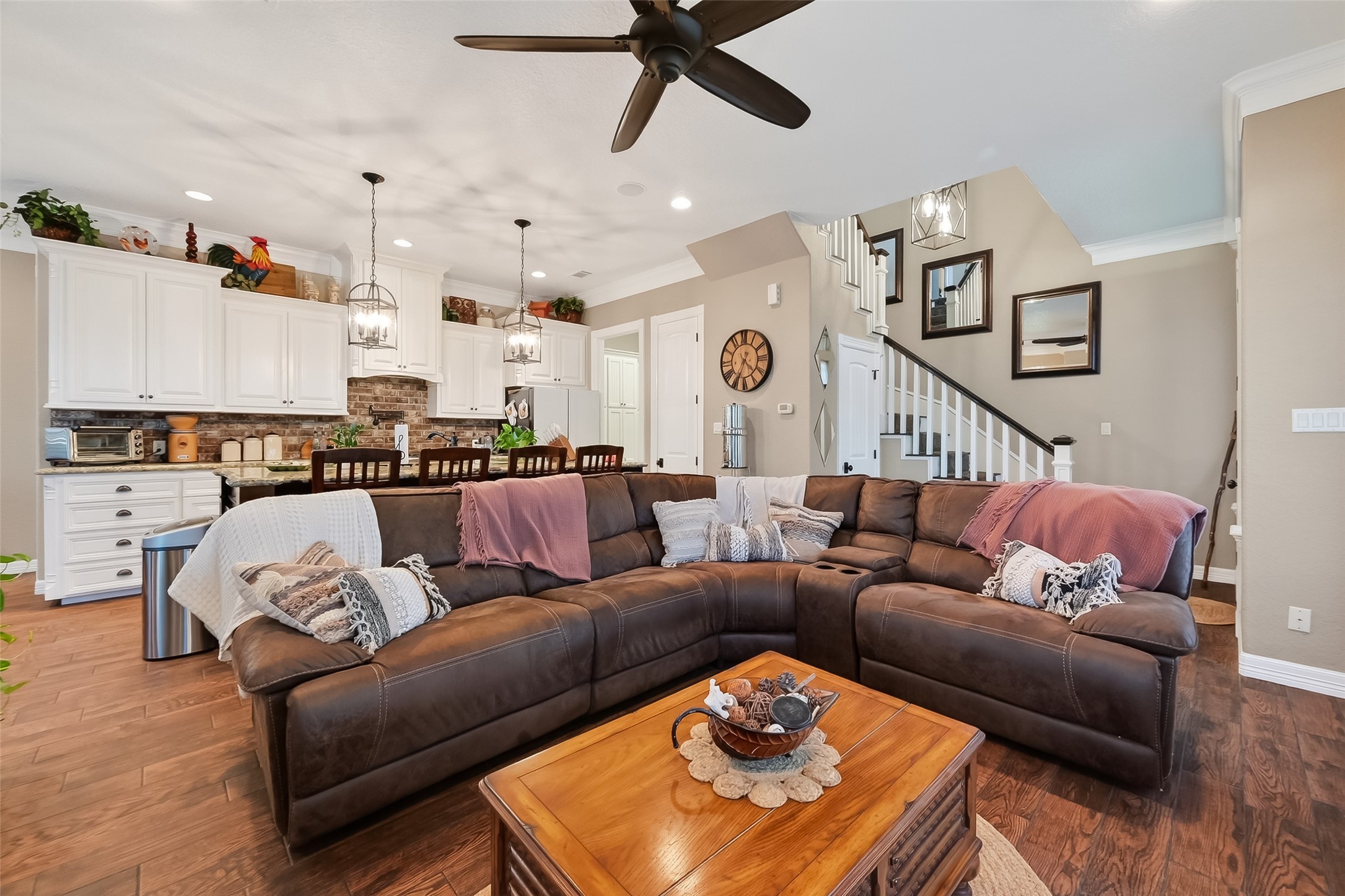 912 County Road 340 Angleton, TX 77515 - Photo 11 of 50 This inviting open-concept living space features a modern ceiling fan. The adjacent kitchen boasts white cabinets, a brick backsplash, and pendant lighting over a breakfast bar. A staircase leads to the upper floor, enhancing the room's spacious feel.