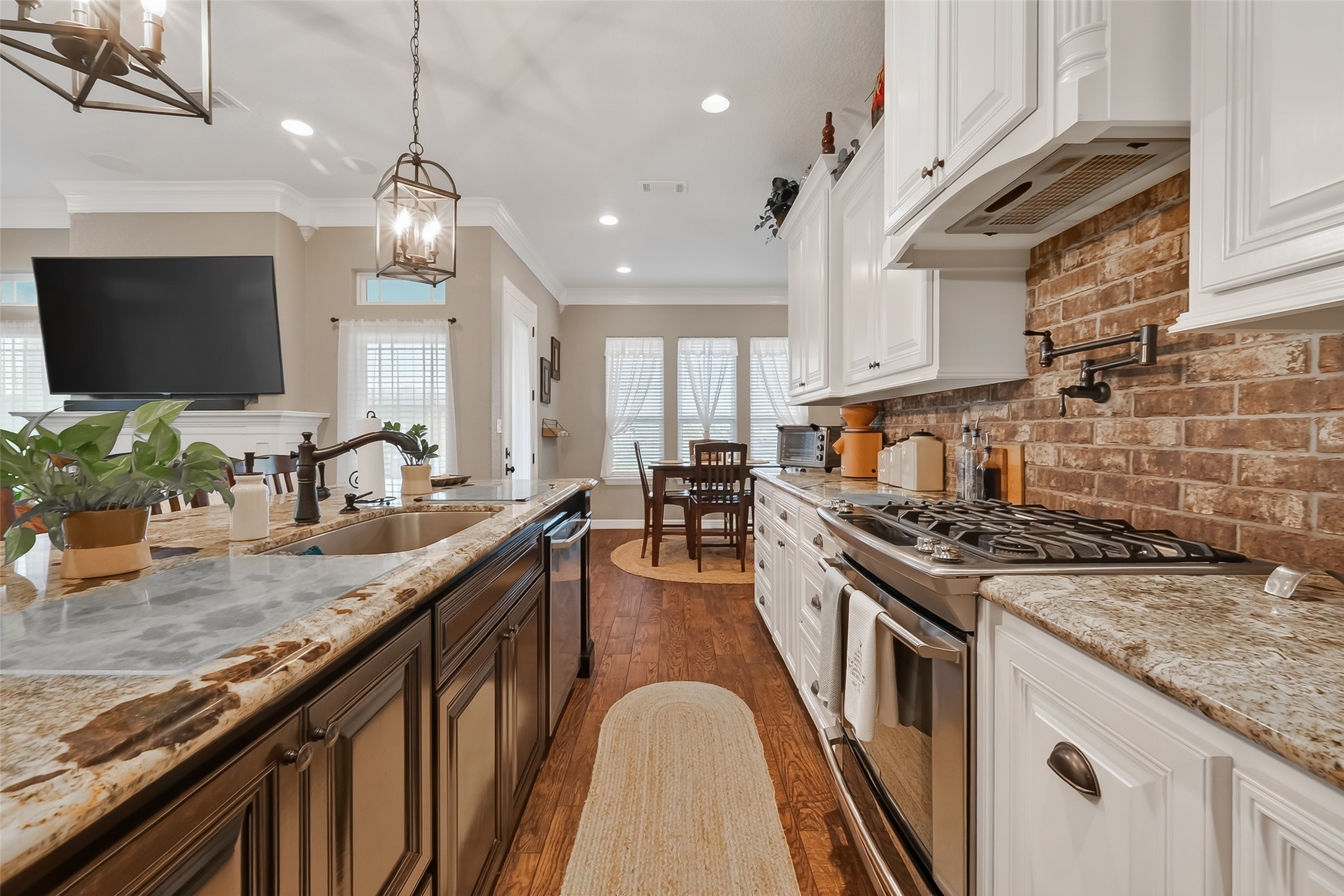 912 County Road 340 Angleton, TX 77515 - Photo 15 of 50 This kitchen features elegant granite countertops and white cabinetry, complemented by a brick backsplash. It includes modern stainless steel appliances, a central island with a sink, and a cozy dining area with natural light streaming through large windows. The warm wood flooring adds to the inviting atmosphere.