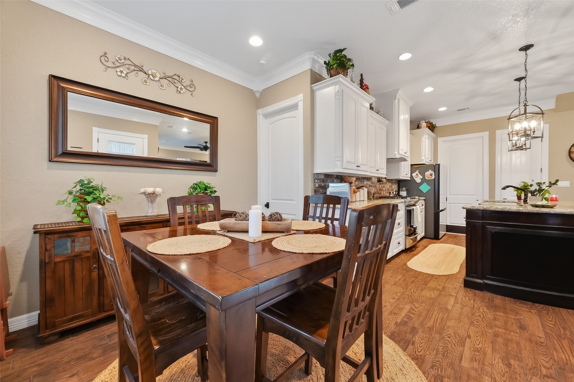 912 County Road 340 Angleton, TX 77515 - Photo 17 of 50 This photo showcases a cozy dining area, adjacent to a modern kitchen. The kitchen features white cabinetry, a dark island, and a stylish light fixture, with warm wood flooring throughout.