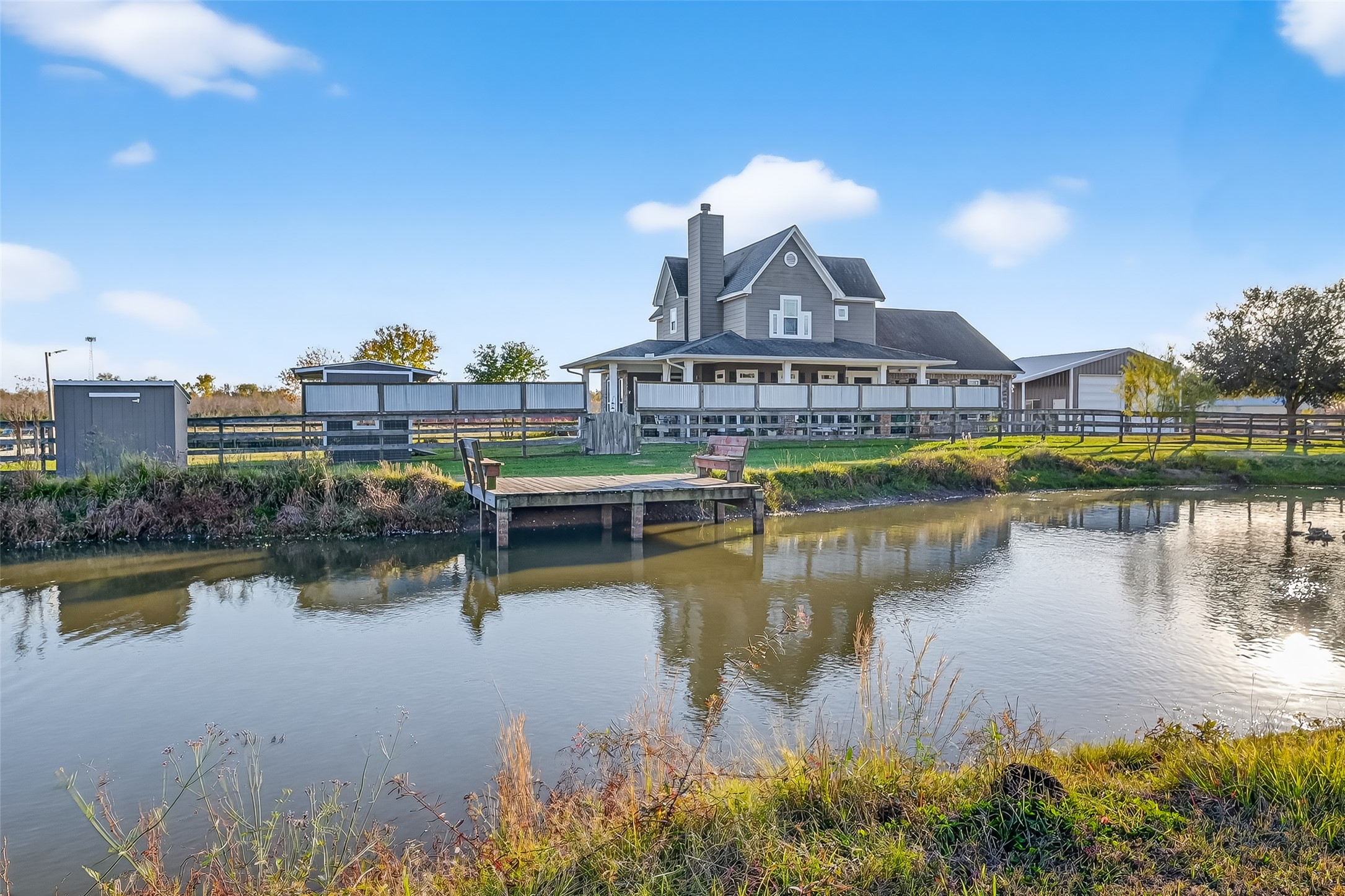 912 County Road 340 Angleton, TX 77515 - Photo 2 of 50 Charming country home with a spacious wrap around porch, nestled beside a serene pond. The property features a fenced area and a small dock, offering picturesque views and a peaceful setting.