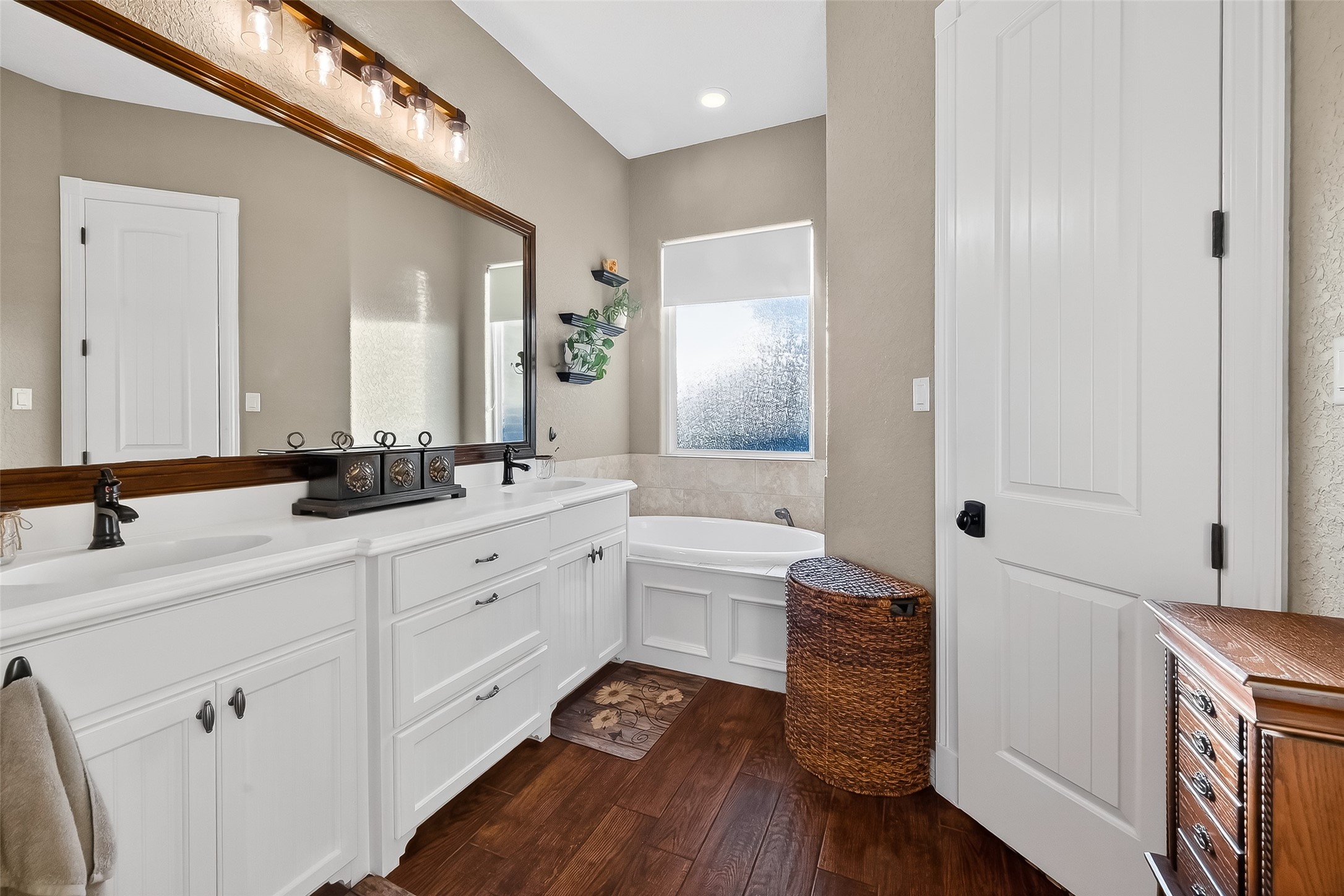 912 County Road 340 Angleton, TX 77515 - Photo 30 of 50 This bathroom features a bright, elegant design with a large double vanity, ample storage, and stylish lighting. It includes a cozy bathtub next to a frosted window, providing privacy and natural light. The wood flooring adds warmth and charm to the space.
