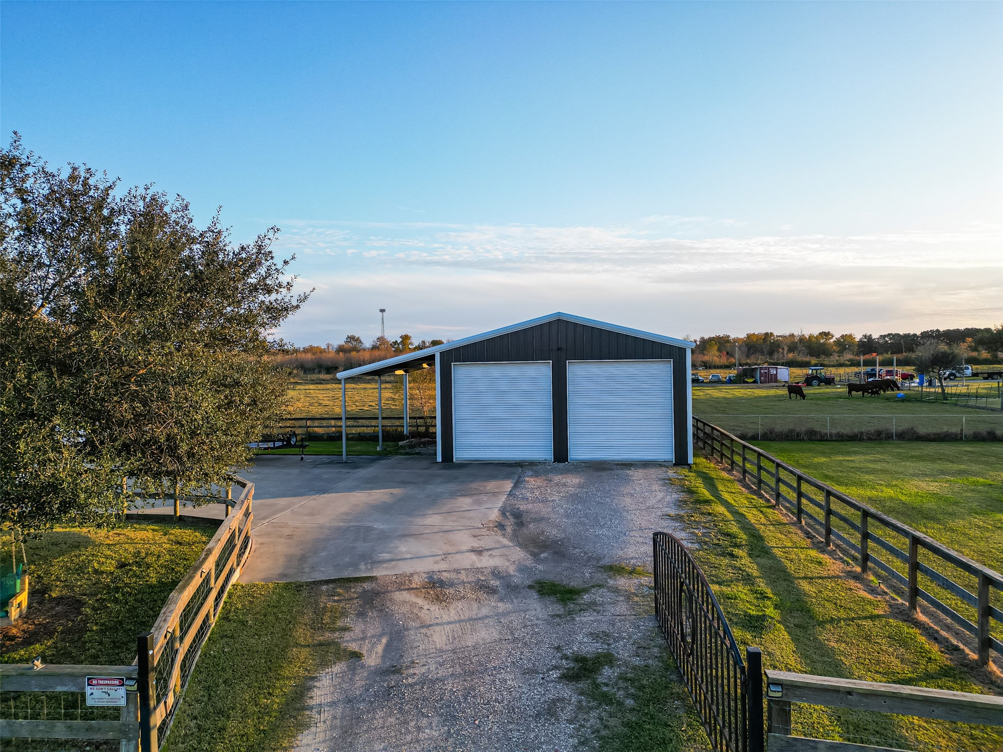 912 County Road 340 Angleton, TX 77515 - Photo 34 of 50 A spacious property featuring a large metal building with two roll-up garage doors, ideal for storage or workshop use. It is surrounded by open fields and fencing, with a paved driveway leading to the building, offering a peaceful rural setting.