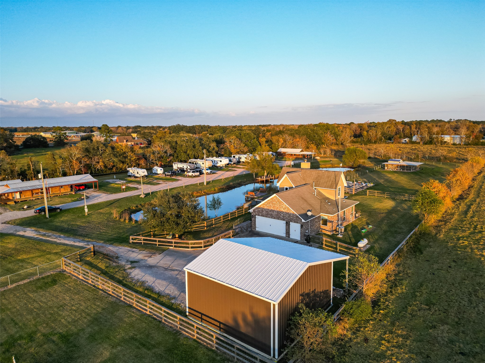 912 County Road 340 Angleton, TX 77515 - Photo 37 of 50 This aerial view showcases a spacious rural property with a charming house, a large barn, and a pond. The expansive land offers ample space and privacy, with surrounding greenery and a well-maintained driveway leading to multiple buildings. Ideal for those seeking a serene country lifestyle.
