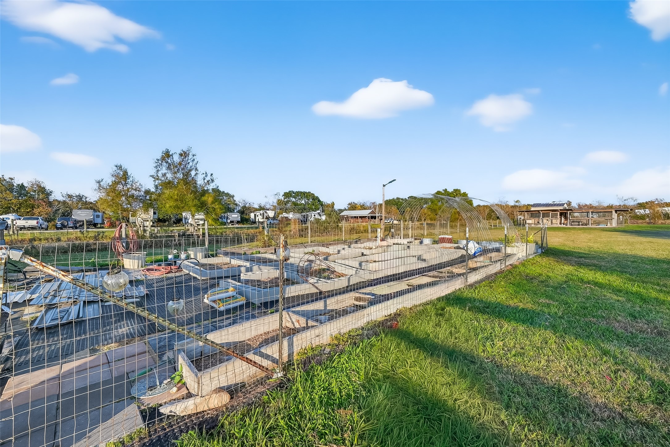 912 County Road 340 Angleton, TX 77515 - Photo 41 of 50 This photo shows a fenced garden area with raised beds under construction, set in a spacious, grassy yard. It’s ideal for outdoor projects or gardening enthusiasts. Additional structures and vehicles can be seen in the background, suggesting a rural or semi-rural setting.