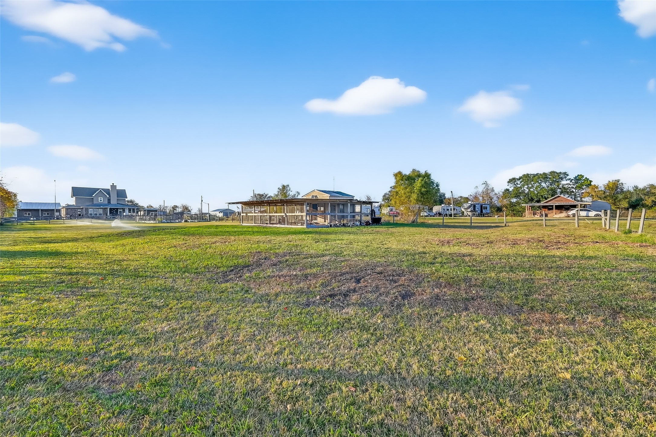 912 County Road 340 Angleton, TX 77515 - Photo 42 of 50 Expansive grassy lot with several structures in the distance, including a covered patio and residential buildings. Ideal for someone seeking a spacious property with development potential. Serene and open setting.