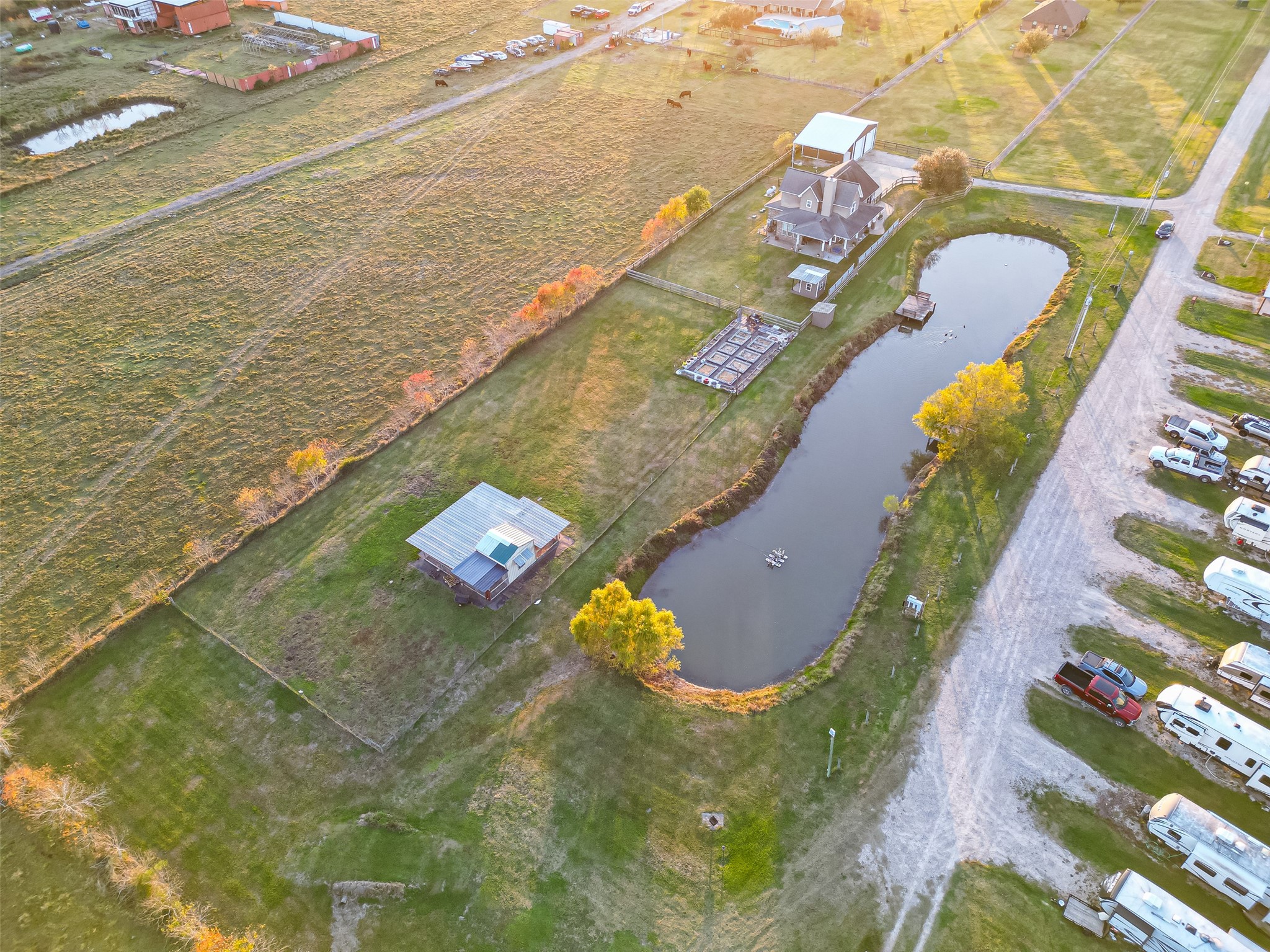 912 County Road 340 Angleton, TX 77515 - Photo 47 of 50 Aerial view of a spacious rural property featuring a large, elegant house with a wrap around porch, adjacent to a long pond. The property includes a separate barn and is surrounded by expansive green fields.