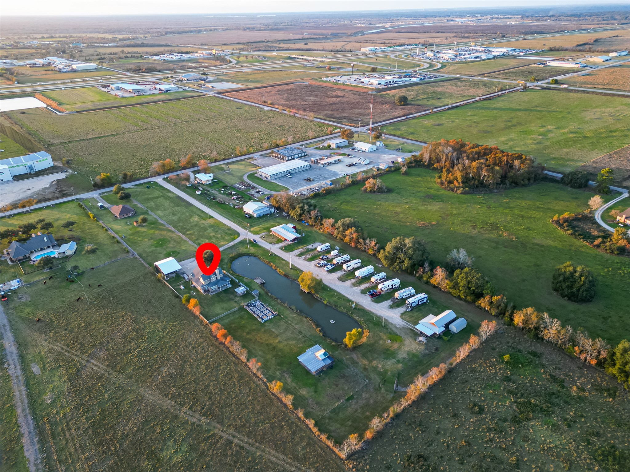 912 County Road 340 Angleton, TX 77515 - Photo 48 of 50 This aerial photo highlights the home marked with a red circle. The house is surrounded by open fields, a pond, and nearby RV parking. The area is tranquil with spacious land and proximity to a few commercial buildings. Ideal for those seeking a peaceful countryside setting.