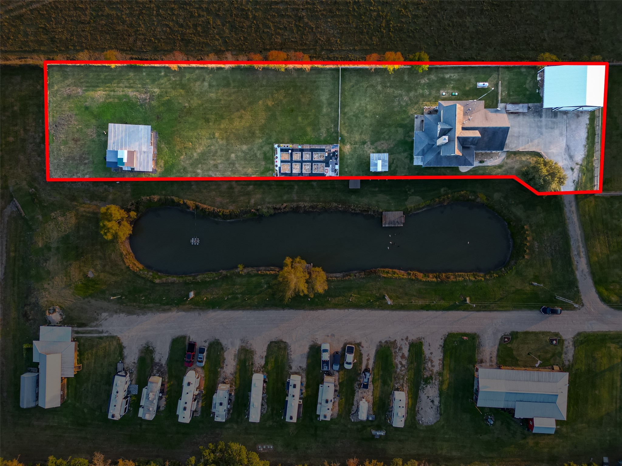 912 County Road 340 Angleton, TX 77515 - Photo 50 of 50 This aerial photo showcases the spacious property outlined in red, featuring a large house with a driveway, a separate building, and ample green space. There's a picturesque pond with a small dock in front of the property, offering a serene landscape.