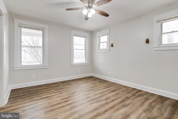 an empty room with wooden floor windows and fan