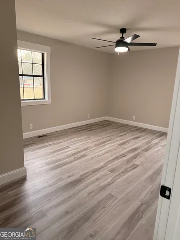 an empty room with wooden floor fan and windows