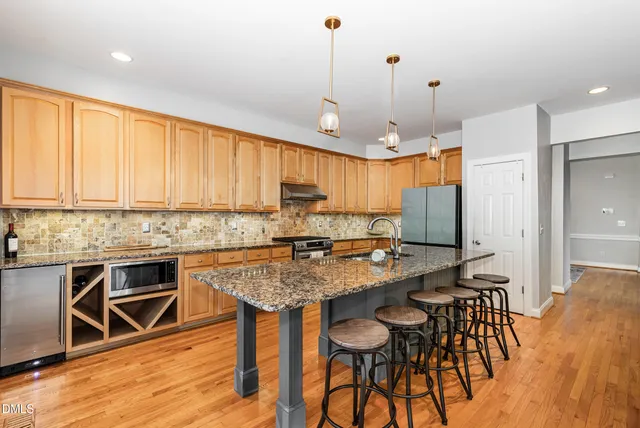 a kitchen with stainless steel appliances granite countertop a stove top oven a refrigerator a sink and white cabinets with wooden floor