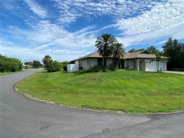 a view of a white house with a big yard plants and large trees