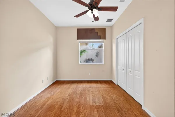 an empty room with wooden floor chandelier fan and windows