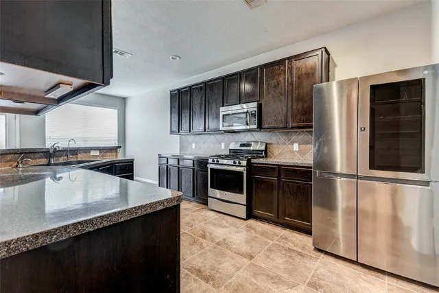 a kitchen with stainless steel appliances granite countertop a stove a sink and a refrigerator with white cabinets