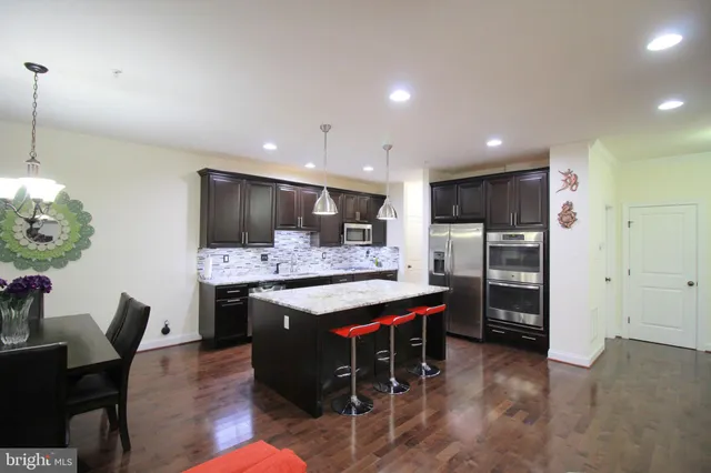 a kitchen with stainless steel appliances kitchen island granite countertop a table chairs and a refrigerator