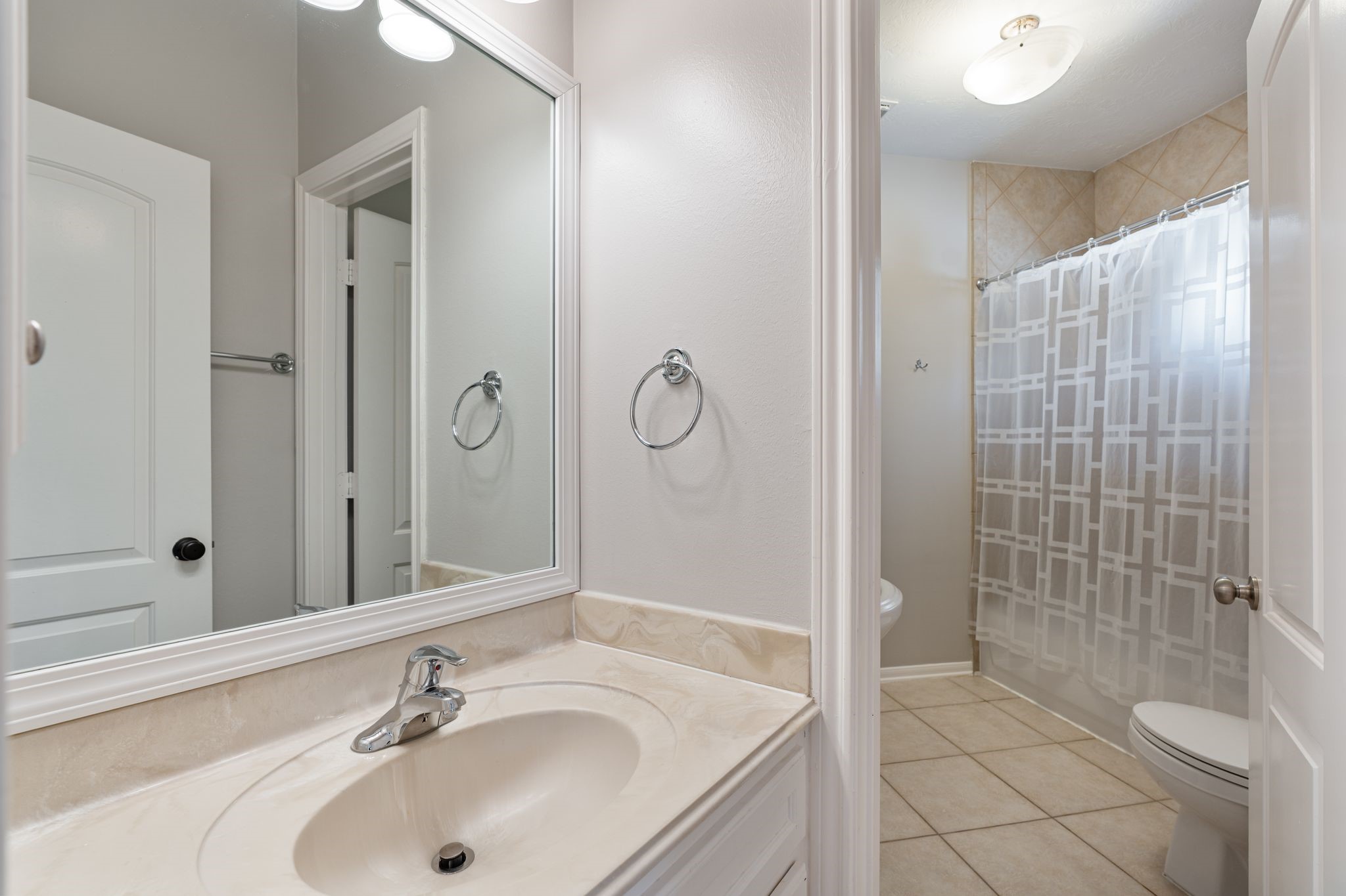 3822 Merrick Street Houston, TX 77025 - Photo 25 of 34 A full hall bath upstairs features a single white vanity with integrated countertop sink, a wide framed mirror with vanity lighting, chrome fixtures, tile flooring, and a tub/shower combo with diagonal tile surround extending to the ceiling.