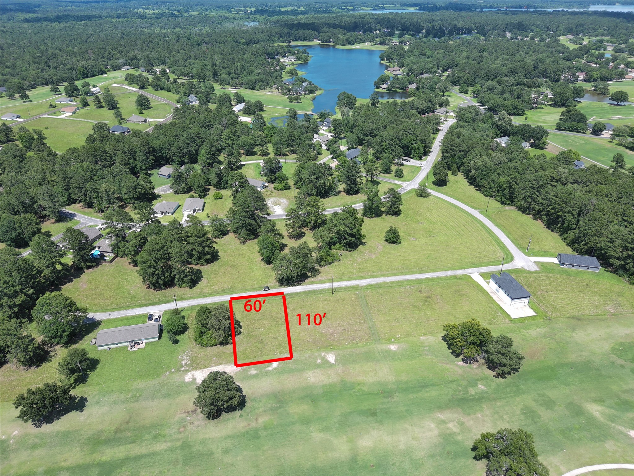 59 Oakridge South Trinity, TX 75862 - Photo 2 of 10 This aerial photo showcases a spacious plot of land, outlined in red, measuring 60 by 110 feet. It is situated in a serene, green residential area with scattered houses and lush trees. The nearby picturesque lake adds to the scenic beauty, making it an ideal location for a tranquil home.