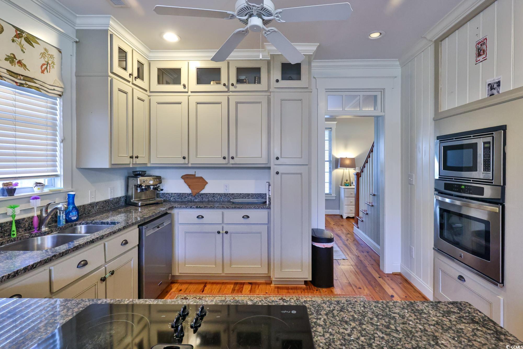 998 Shipmaster Avenue Myrtle Beach, SC 29579 - Photo 13 of 40 Kitchen featuring dark stone counters, appliances with stainless steel finishes, crown molding, light wood finished floors, and glass insert cabinets