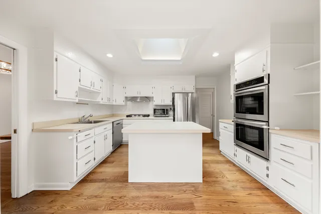 a kitchen with stainless steel appliances a stove top oven a sink a refrigerator white cabinets and wooden floor