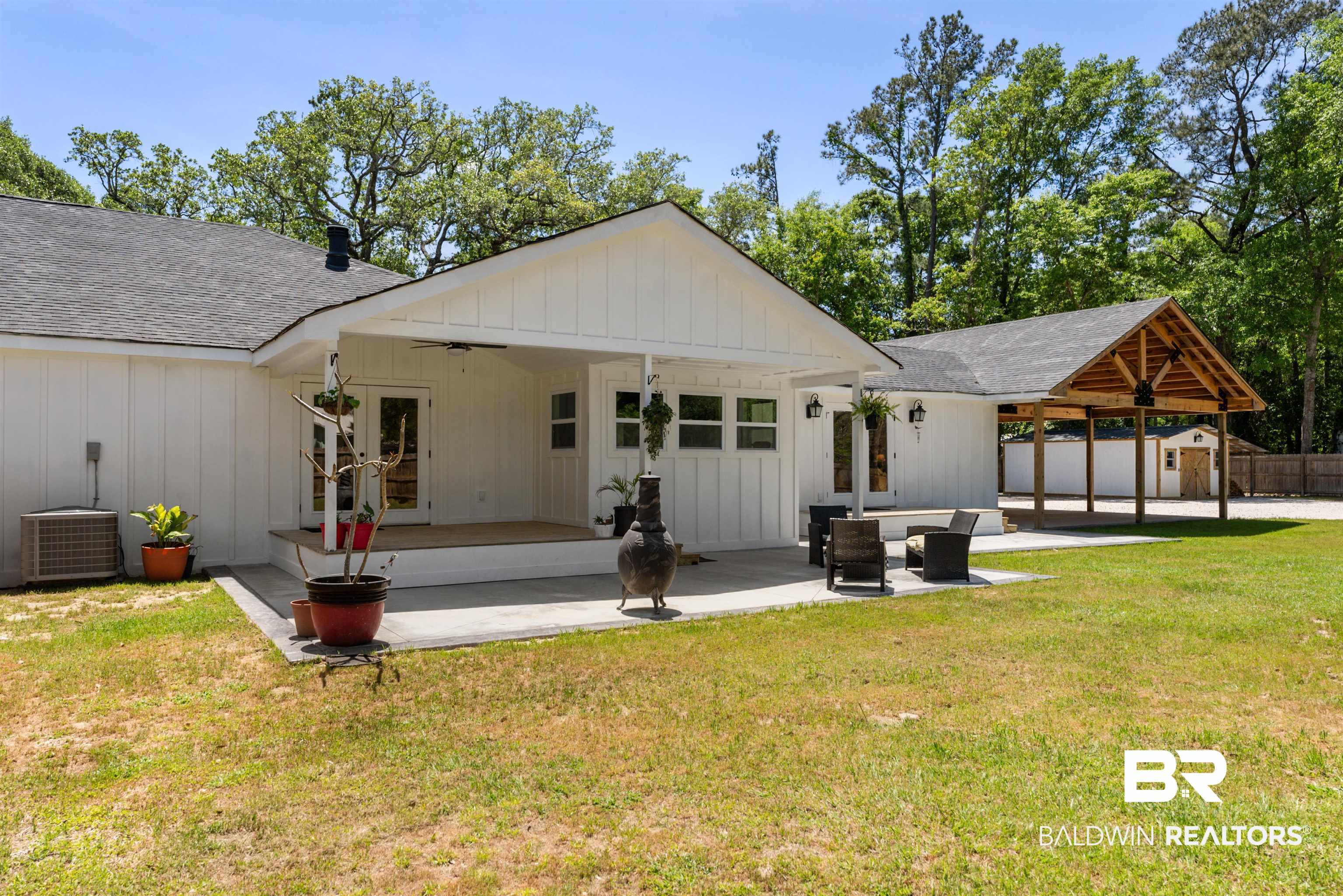 6447 Bemis Lane Bon Secour, AL 36511 - Photo 8 of 62 Rear exterior featuring white board-and-batten siding, a covered patio with a wood deck, a concrete patio area, and a separate covered carport structure with exposed wood beams