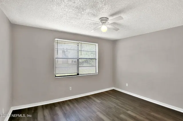 an empty room with wooden floor chandelier fan and windows