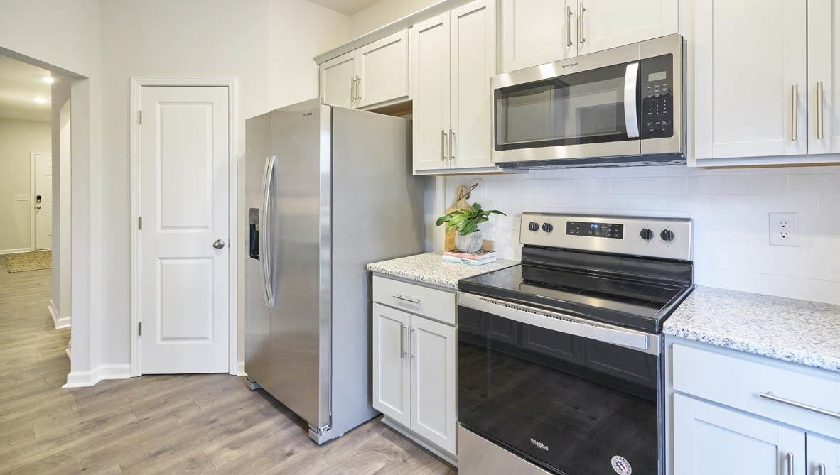 a kitchen with stainless steel appliances granite countertop white cabinets a stove a microwave and a refrigerator