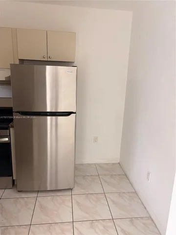 a view of a refrigerator in kitchen and an empty room
