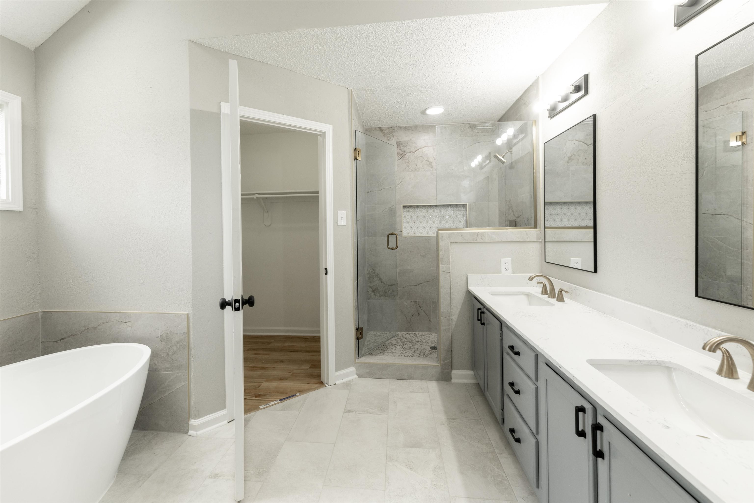 7421 Richmond Road Memphis, TN 38125 - Photo 23 of 39 Spacious bathroom featuring a freestanding soaking tub, a double vanity with light gray cabinetry and white countertops, a walk-in shower with glass enclosure and tiled walls, and light tile flooring