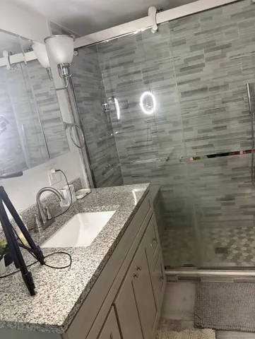 a bathroom with a granite countertop sink a mirror and shower