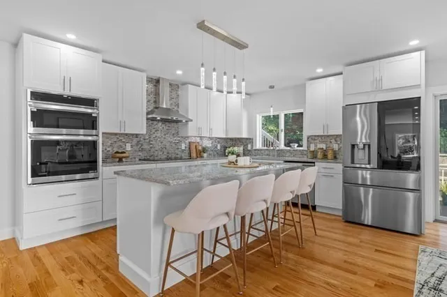 a kitchen with stainless steel appliances granite countertop a stove a sink a refrigerator and white cabinets with wooden floor