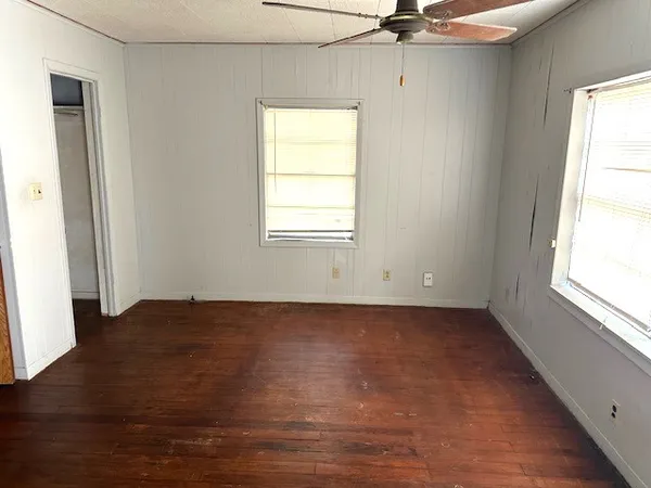 an empty room with wooden floor fan and windows