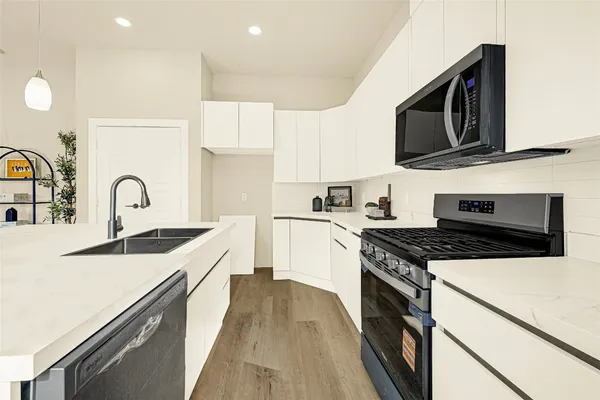 a kitchen with stainless steel appliances granite countertop a stove top oven a sink dishwasher and white cabinets with wooden floor