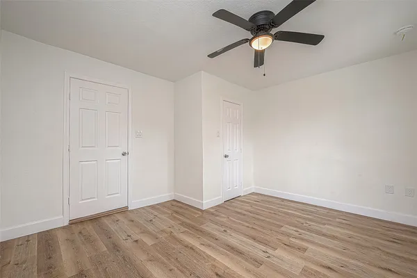 an empty room with wooden floor ceiling fan and windows