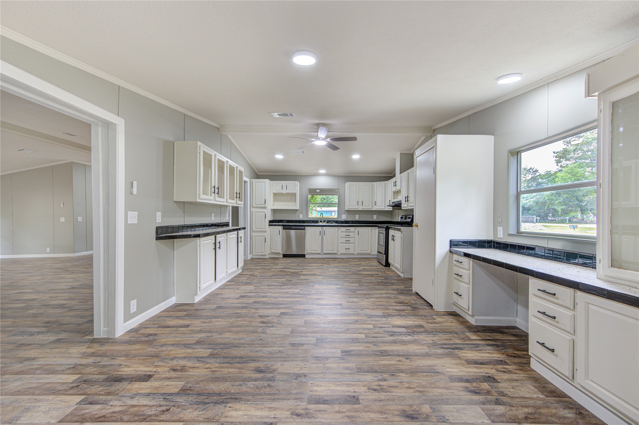 30226 Davis Street Magnolia, TX 77355 - Photo 16 of 50 This photo showcases a spacious, modern kitchen with ample cabinet space, large windows, and wood-style flooring. The kitchen features sleek countertops, a ceiling fan, and an open layout that flows into the adjoining room.