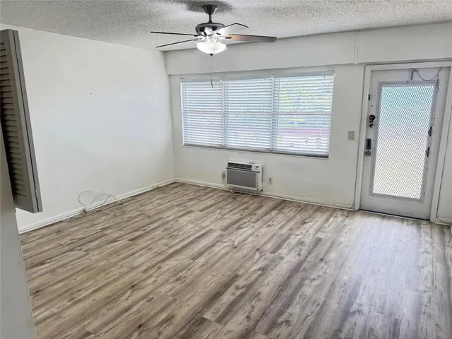 an empty room with wooden floor chandelier fan and windows
