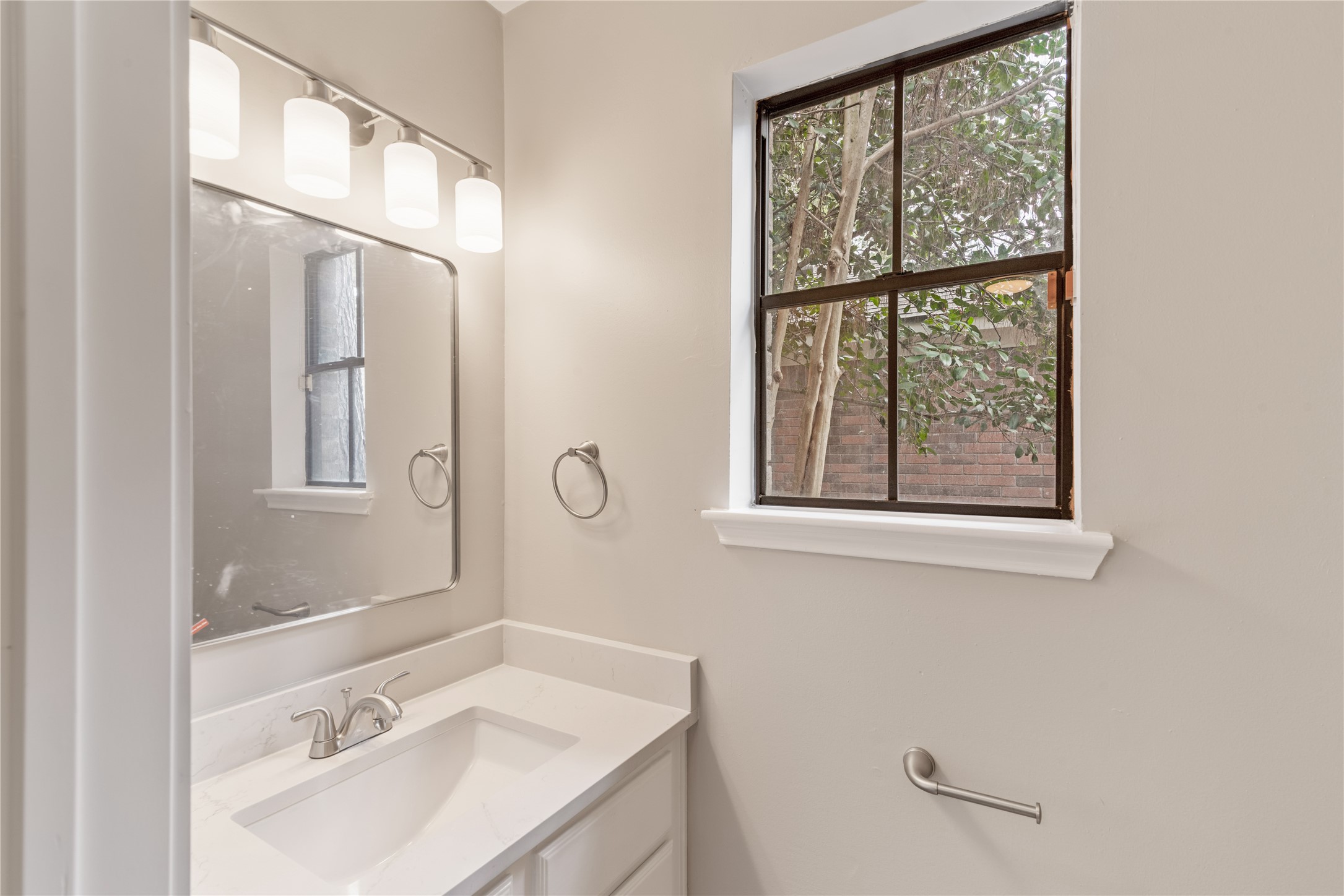 10 White Fawn Drive Spring, TX 77381 - Photo 16 of 26 This primary bathroom features a modern vanity with a sleek countertop, a large mirrors, and stylish lighting. A window provides natural light and a view of greenery outside, creating a bright and inviting space.