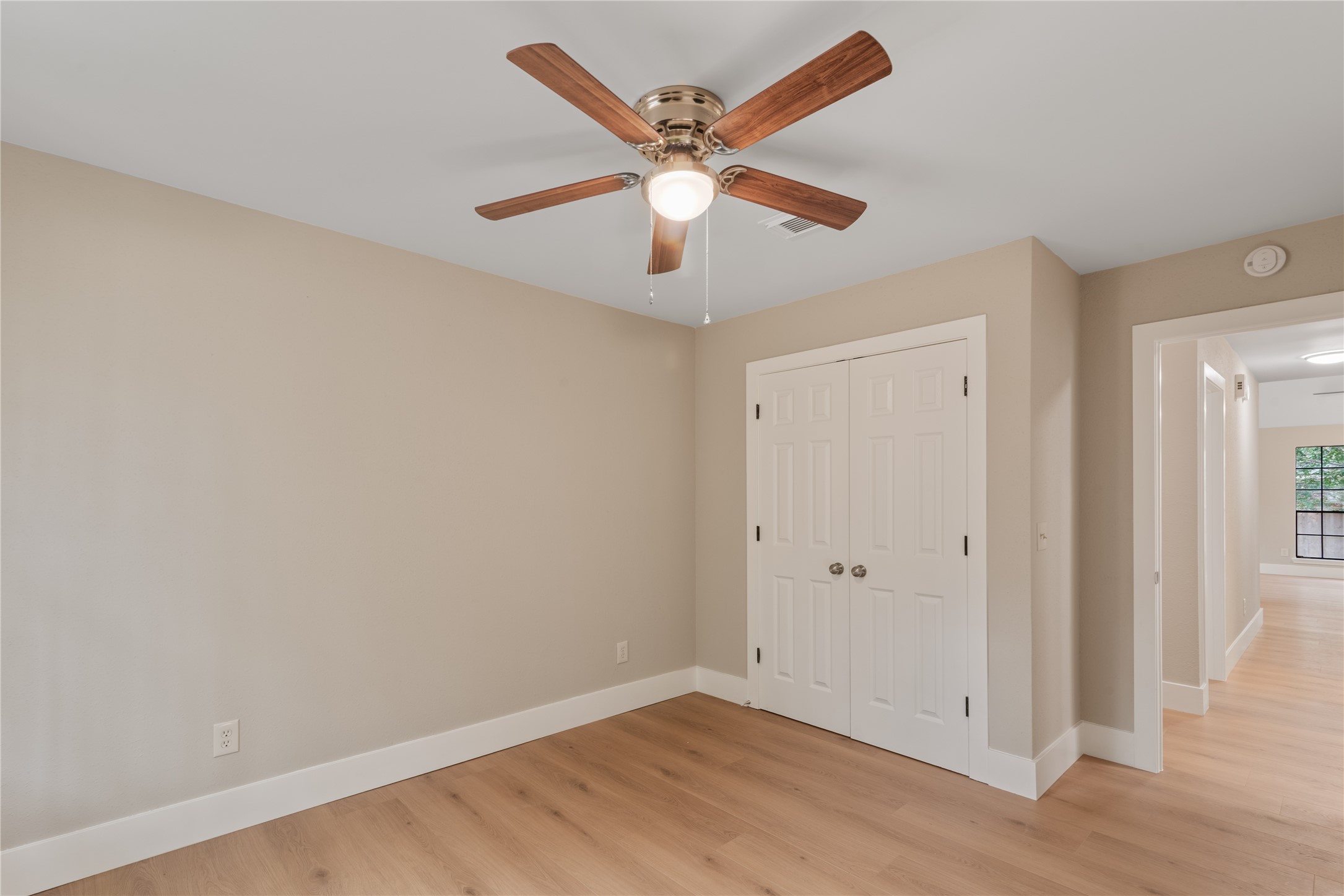 10 White Fawn Drive Spring, TX 77381 - Photo 18 of 26 This room features a neutral color palette with light wood flooring and a ceiling fan. It includes a double-door closet and connects to a hallway leading to another room with large windows.