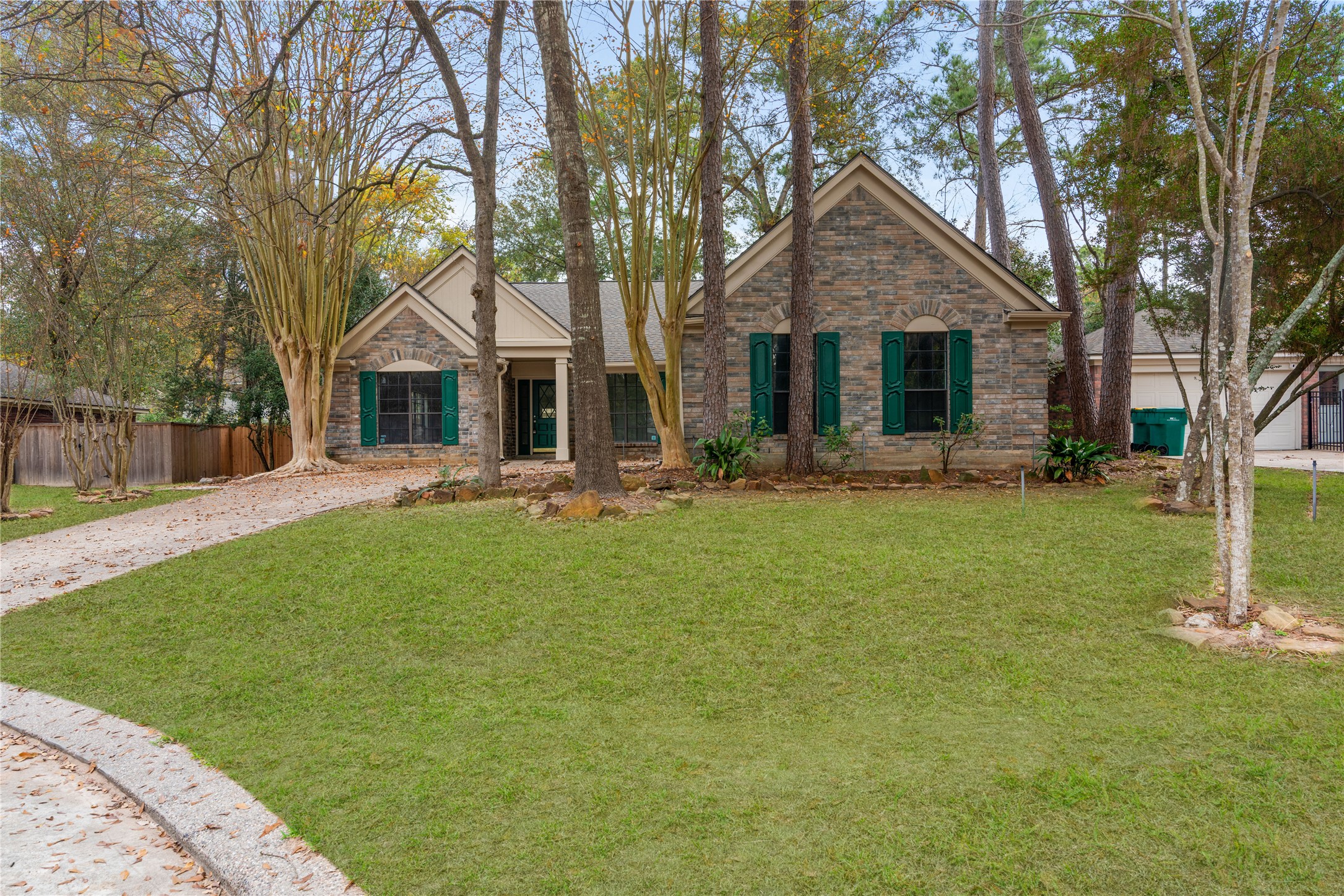 10 White Fawn Drive Spring, TX 77381 - Photo 2 of 26 Color enhanced. This charming home features a classic brick facade with green shutters, nestled among mature trees. The spacious front yard offers a welcoming pathway leading to the entrance, promising a serene and picturesque setting.