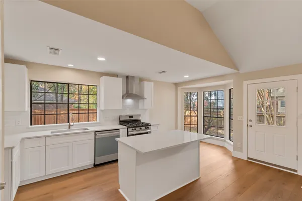a large white kitchen with granite countertop a stove a sink a refrigerator and white cabinets with wooden floor