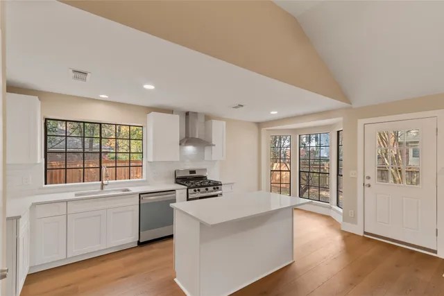 a large white kitchen with granite countertop a stove a sink a refrigerator and white cabinets with wooden floor