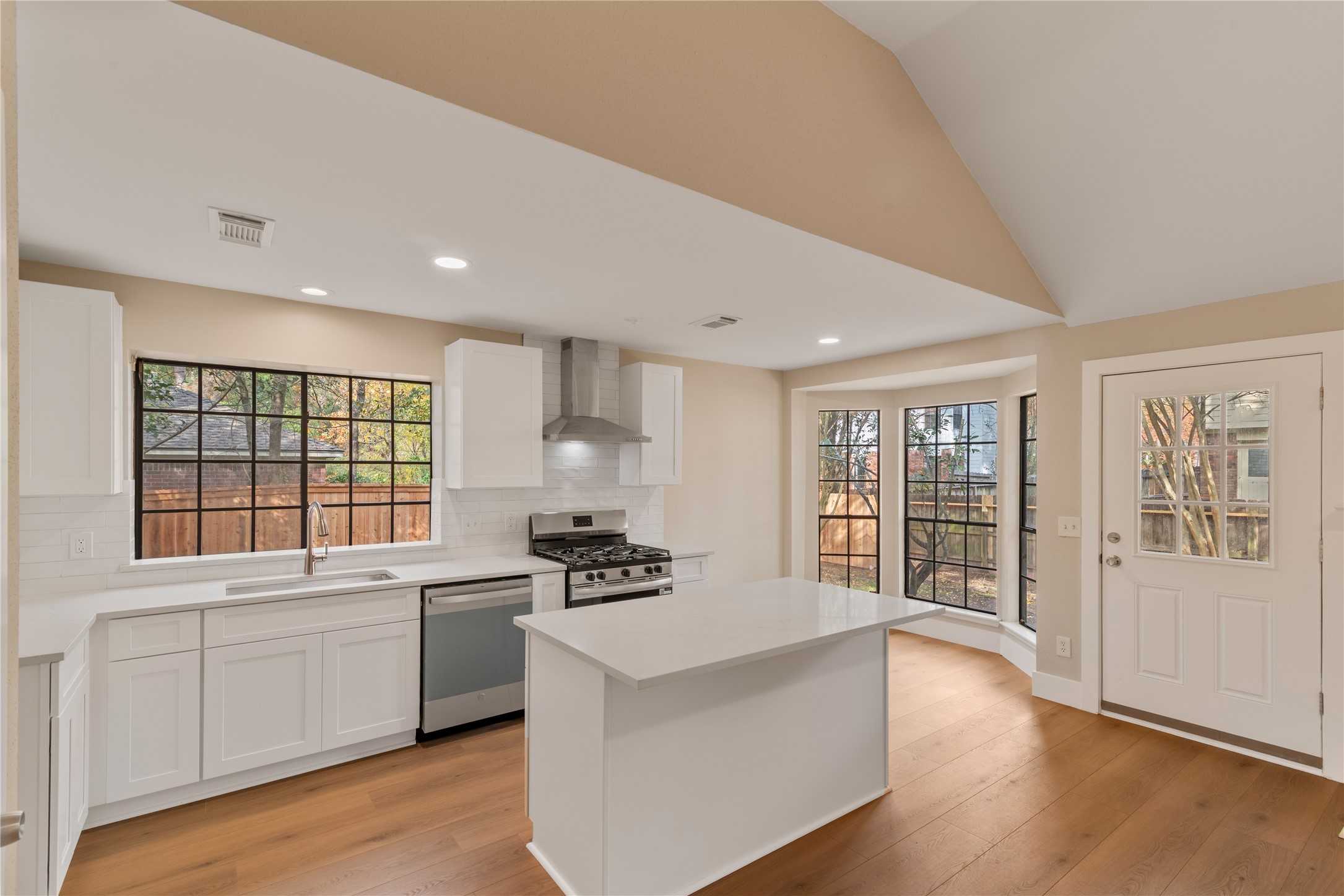 10 White Fawn Drive Spring, TX 77381 - Photo 9 of 26 This kitchen features bright natural light, modern white cabinetry, and stainless steel appliances. It has a central island, large windows with a view of the backyard, and warm wooden floors, creating an inviting and functional space.