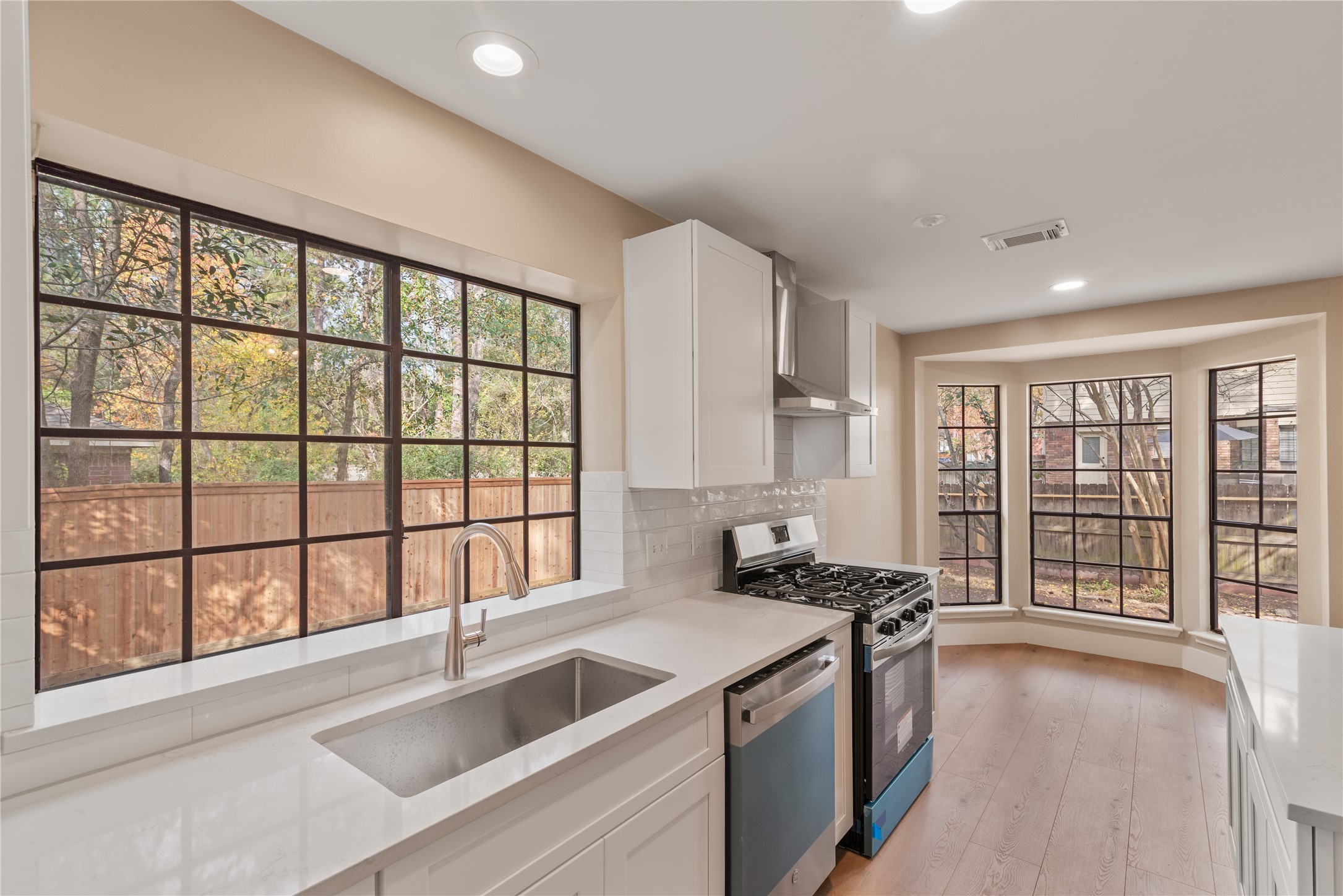 10 White Fawn Drive Spring, TX 77381 - Photo 10 of 26 Modern kitchen featuring large windows for natural light, sleek white cabinetry, a stainless steel sink, and a gas stove. The light wood flooring and neutral palette create an inviting space.