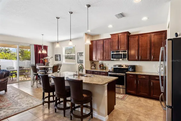 a kitchen with stainless steel appliances granite countertop a sink a stove a refrigerator a dining table and chairs with wooden floor