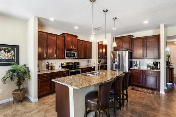 a kitchen with stainless steel appliances kitchen island granite countertop a stove refrigerator a oven a sink a dining table and chairs with wooden floor