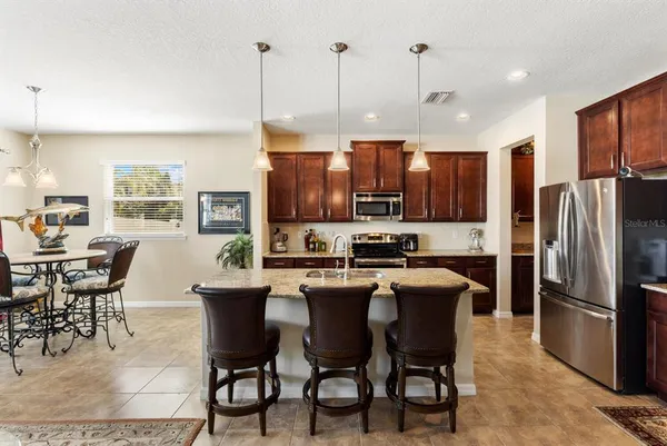 a kitchen with stainless steel appliances granite countertop a sink a stove a refrigerator cabinets a dining table and chairs