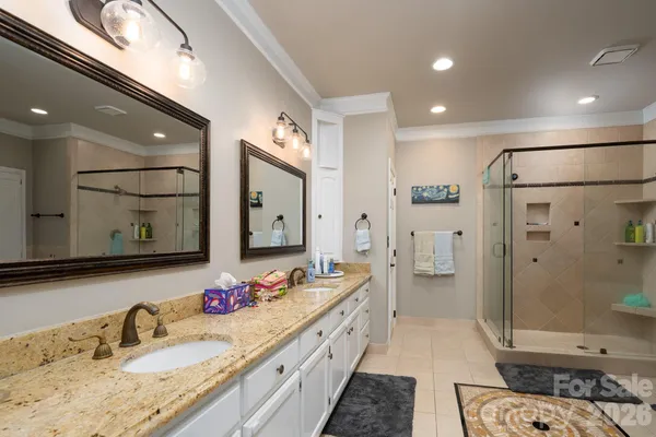a bathroom with a granite countertop double vanity sink a mirror and shower